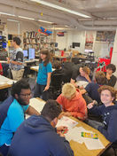 Students in a classroom, talking and working around tables in New York Harbor School