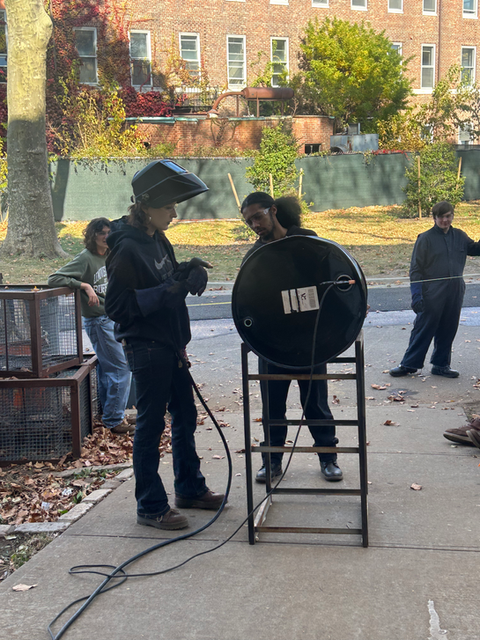 Students welding metal drum outdoors