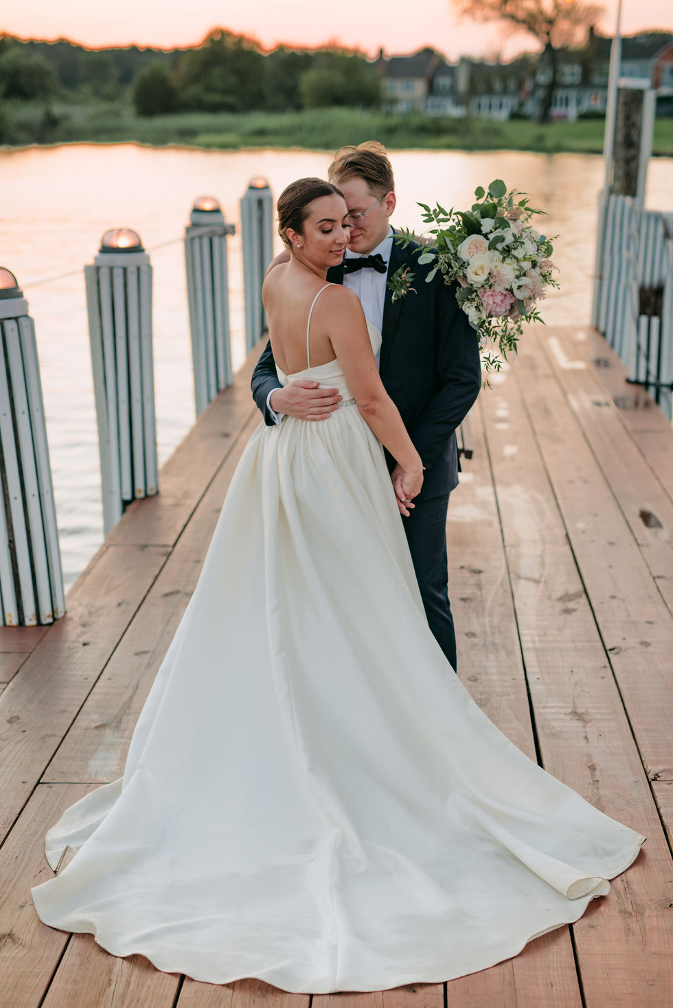 a bride and groom pose for a picture on a dock