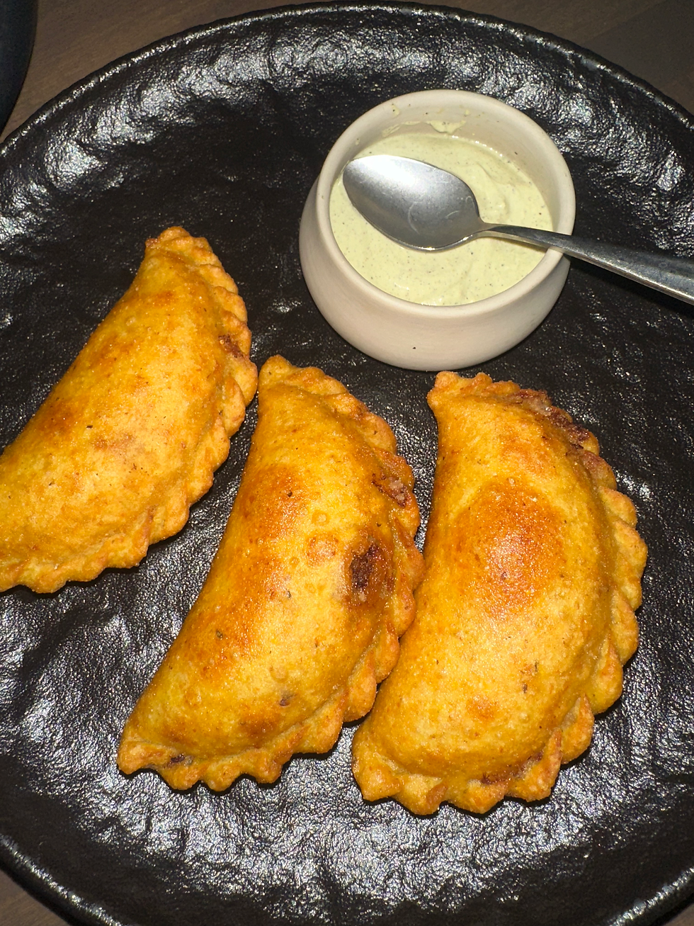 Golden brown empanadas filled with wagyu beef, poblano peppers, and cheese, served on a decorative plate.