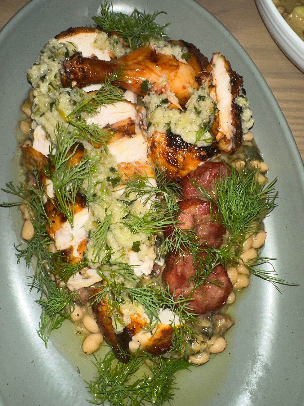 Half Chicken a la Brasa with andouille, navy beans, salsa verde, and fresh herbs at Maxwells Trading.