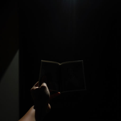 A cinematic, high-contrast image showing a person holding a photo or photo book in a dimly