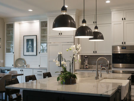 Modern kitchen with white cabinets, Nacarado countertops, and stainless steel appliances. Dark pendant lights hang over the island.