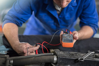 A mechanic in a blue uniform uses a multimeter to check an engine.