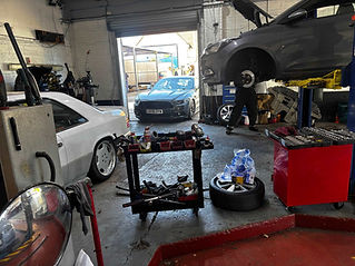 Car repair garage with three cars. A gray car on a lift, wheel removed.