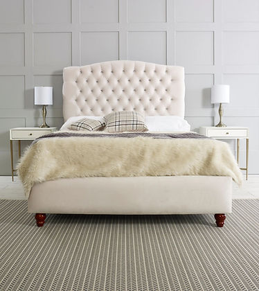 Plush, beige bed with tufted headboard, two plaid pillows, and a fluffy fur blanket.