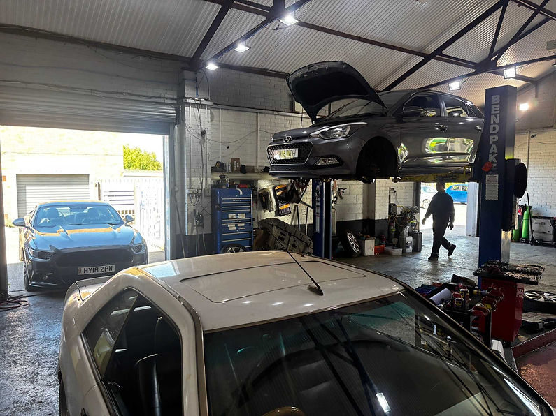Inside a Garage , a gray car is on a lift with a mechanic working.