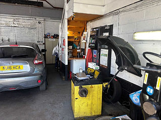 A gray car is parked inside a garage. Nearby, a yellow tire balancing machine and tools
