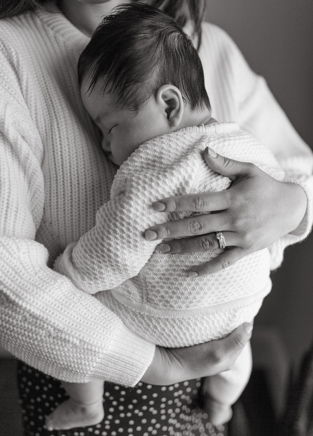 A newborn sleeps in his mother's arms during their in-home newborn session.