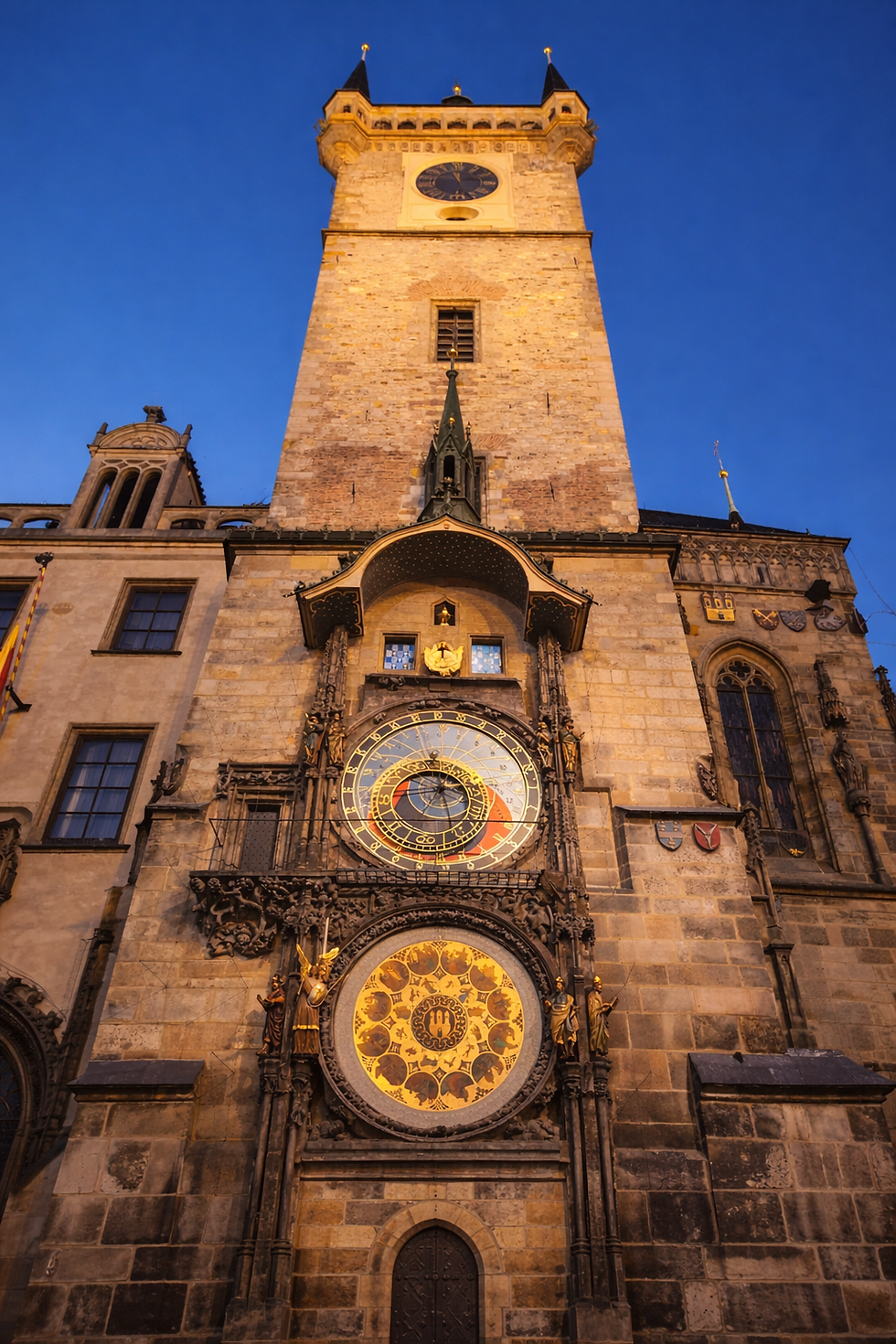 Historic clock tower with ornate astronomical clock, detailed stone facade, and a blue evening sky backdrop, exuding a medieval charm.