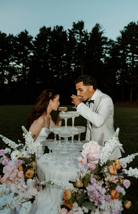 Couple toasting champagne tower, outdoor event with flowers and greenery, home. Giuberti Decor
