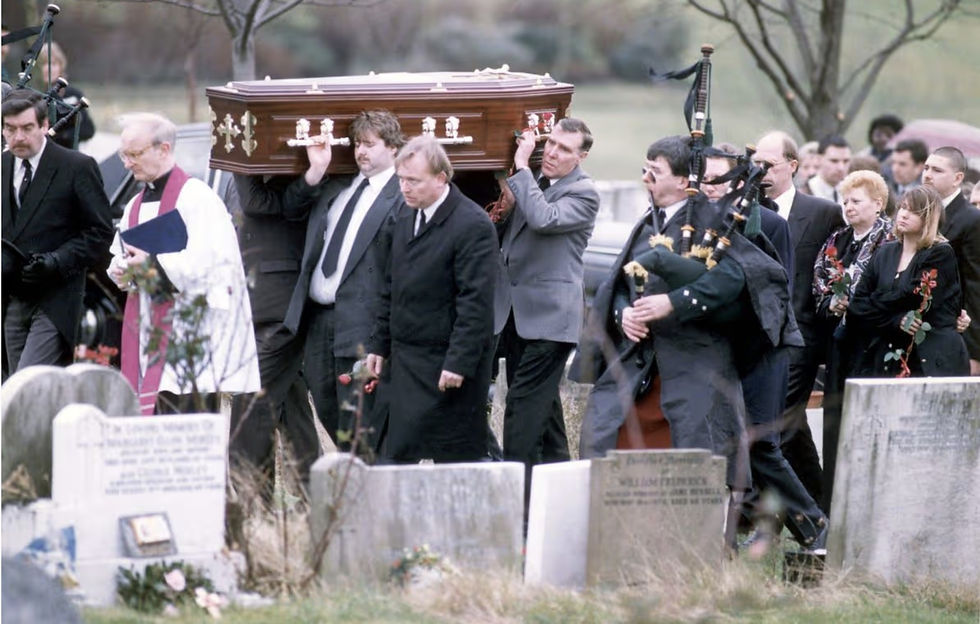 Pallbearers carry a brown coffin through a cemetery as mourners and bagpipers follow, somber and respectful.