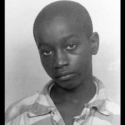 Young person in a striped shirt gazes solemnly at the camera against a plain background. The mood is somber.