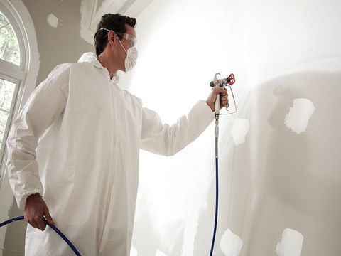 Hombre aplicando pintura con máquina pulverizadora en pared , logrando un acabado uniforme y profesional 