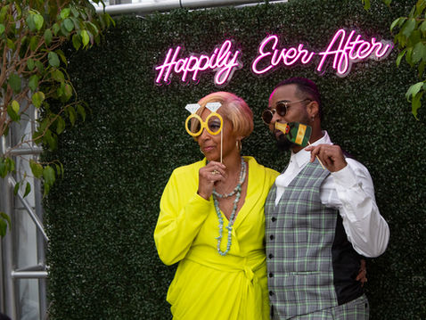 Custom photobooth decor with neon "Happily Ever After" sign and green hedge wedding photo backdrops for premium, interactive elegant photo setups.