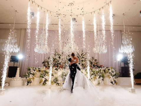 Bride and groom sharing their first dance surrounded by indoor cold sparks, low-lying fog, and falling confetti at a luxury wedding venue