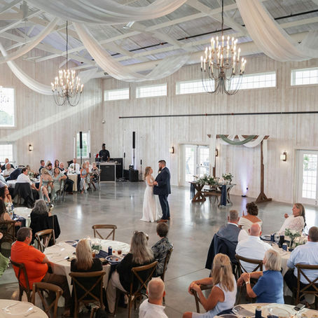 Elegant bride and groom dancing on a luxury wedding reception dance floor surrounded by guests and warm lighting.