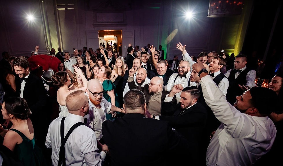 A high-energy overhead shot of guests in formal wedding attire singing and dancing on a crowded dance floor with cinematic lighting.