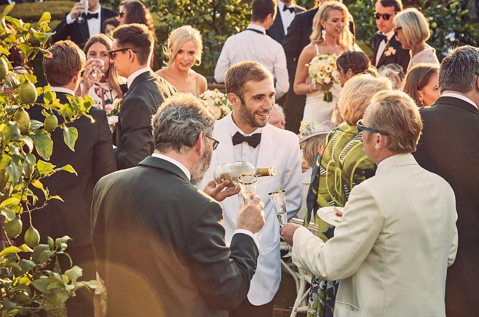 Guests in formal attire enjoying champagne and conversation at an outdoor wedding cocktail hour with lemon trees in the foreground.