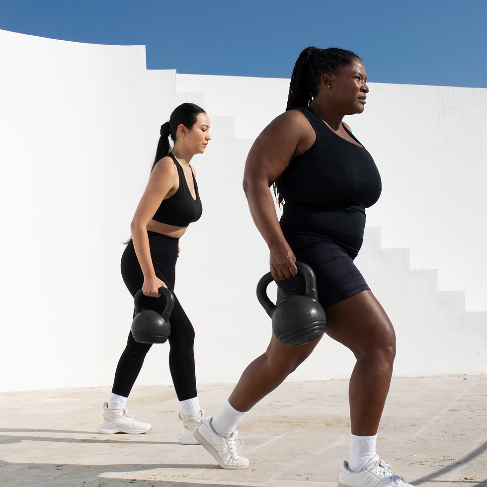 Two women in black workout clothes lunge outdoors, each holding a kettlebell, against a white wall and blue sky.