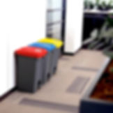 Side on view of a row of three 45 litre pedal bins side by side, grey base, with a red lid, a yellow lid and a blue lid
