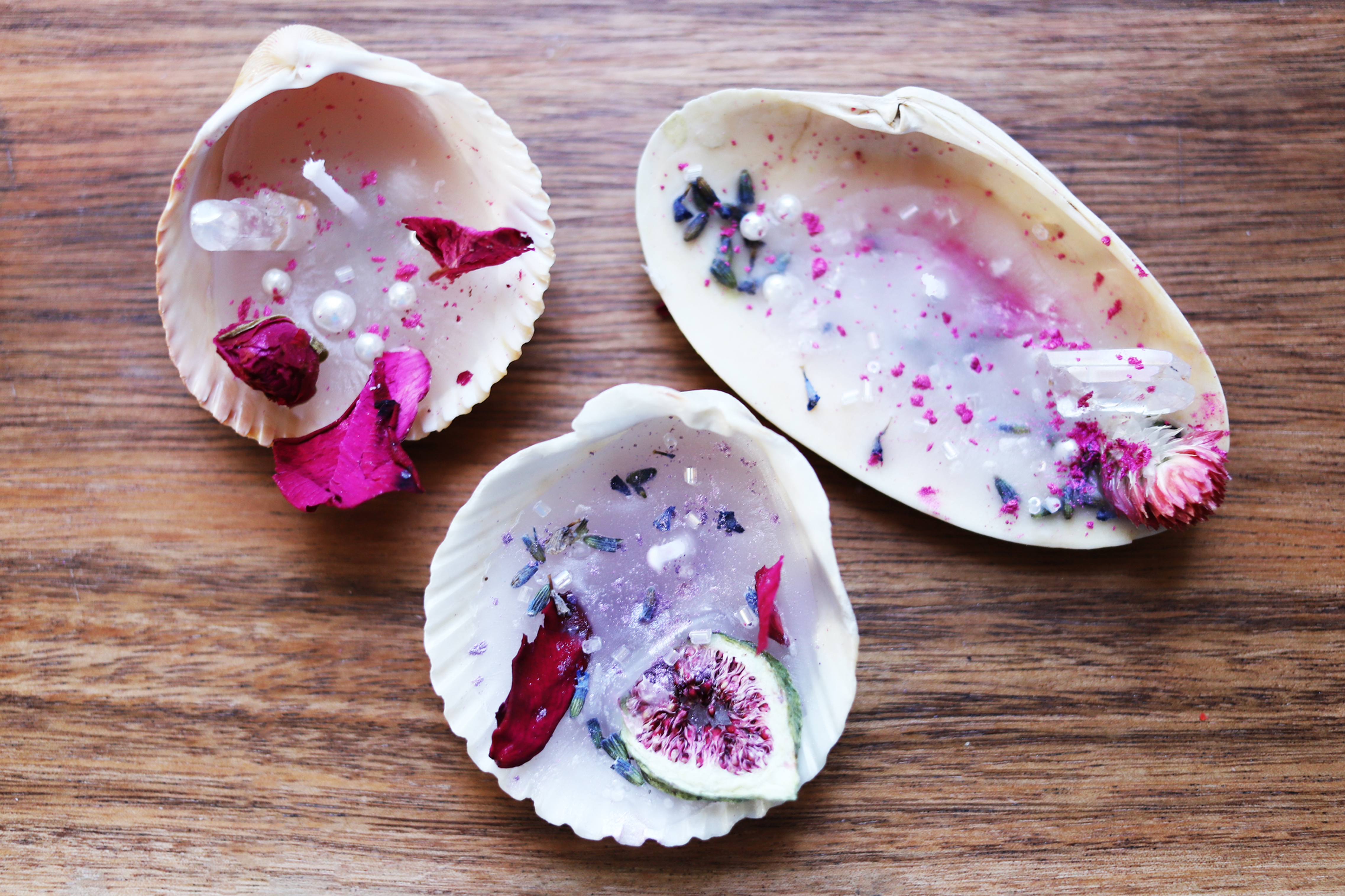 Three seashell candles with floral decorations on a wooden table.