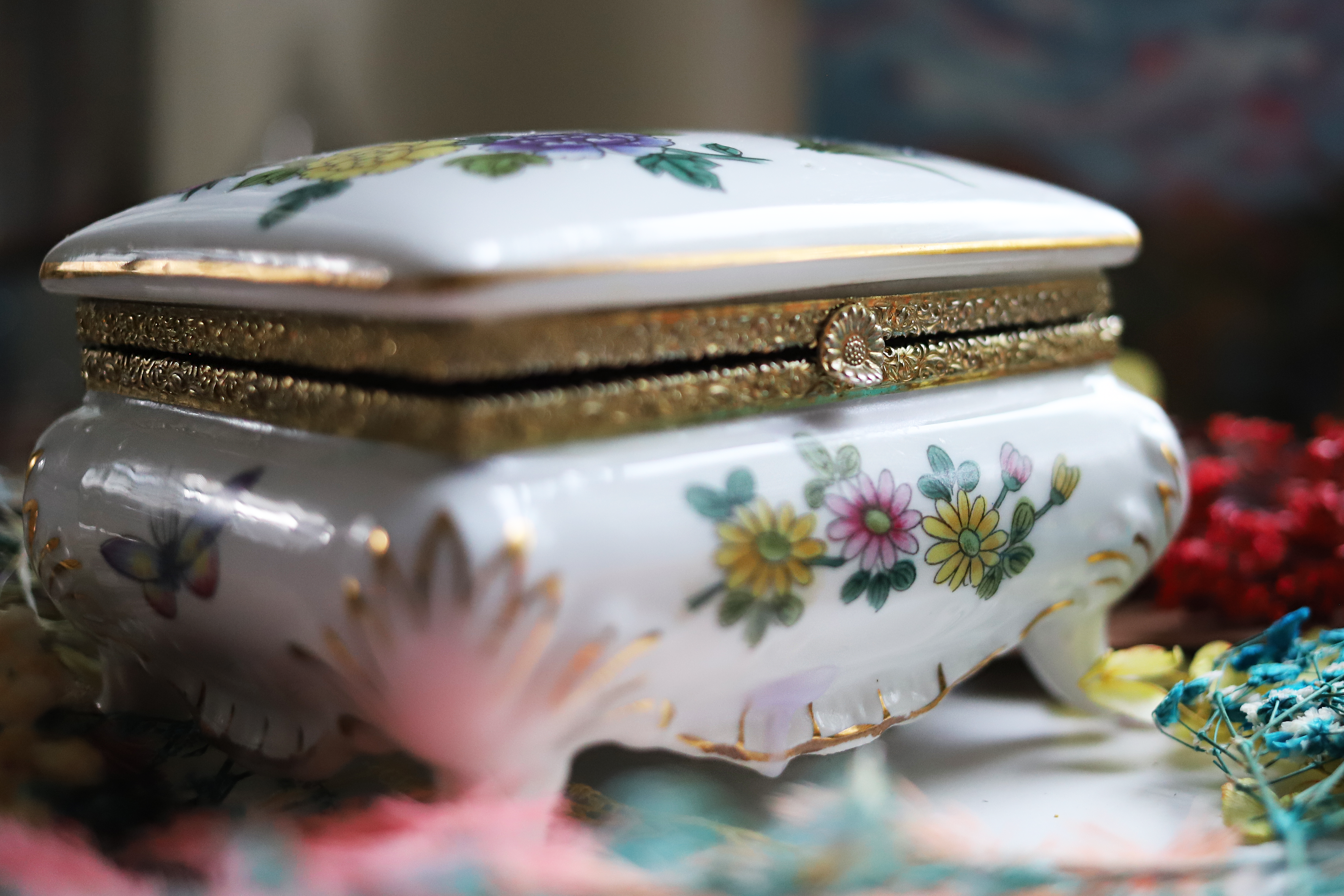 A small white decorative box with gold trim and floral detail