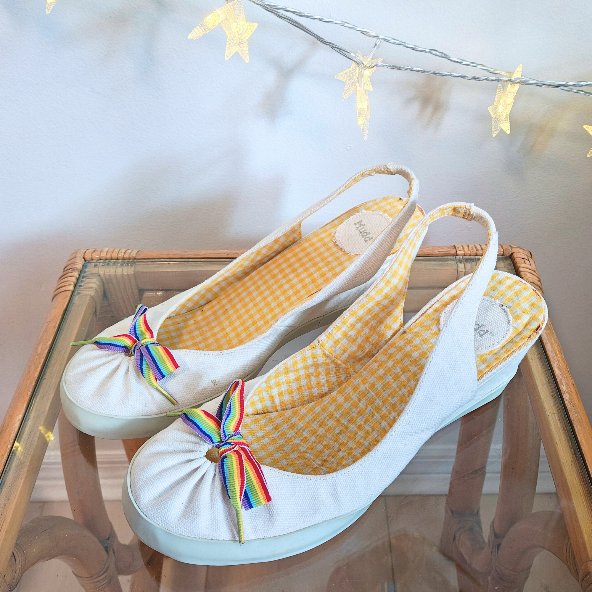 White slingback shoes with rainbow bow on display against white background.