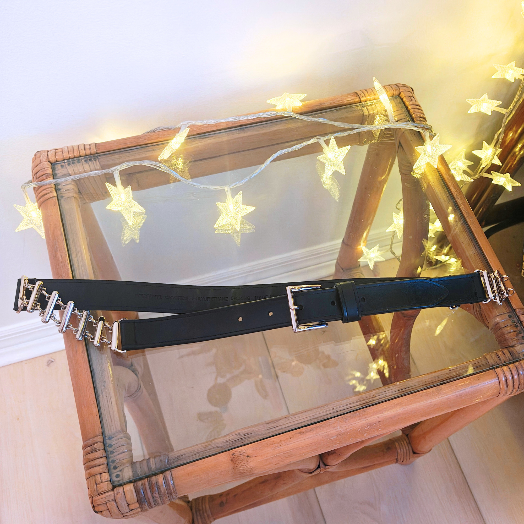 Black belt with silver buckle resting on glass table with lights.