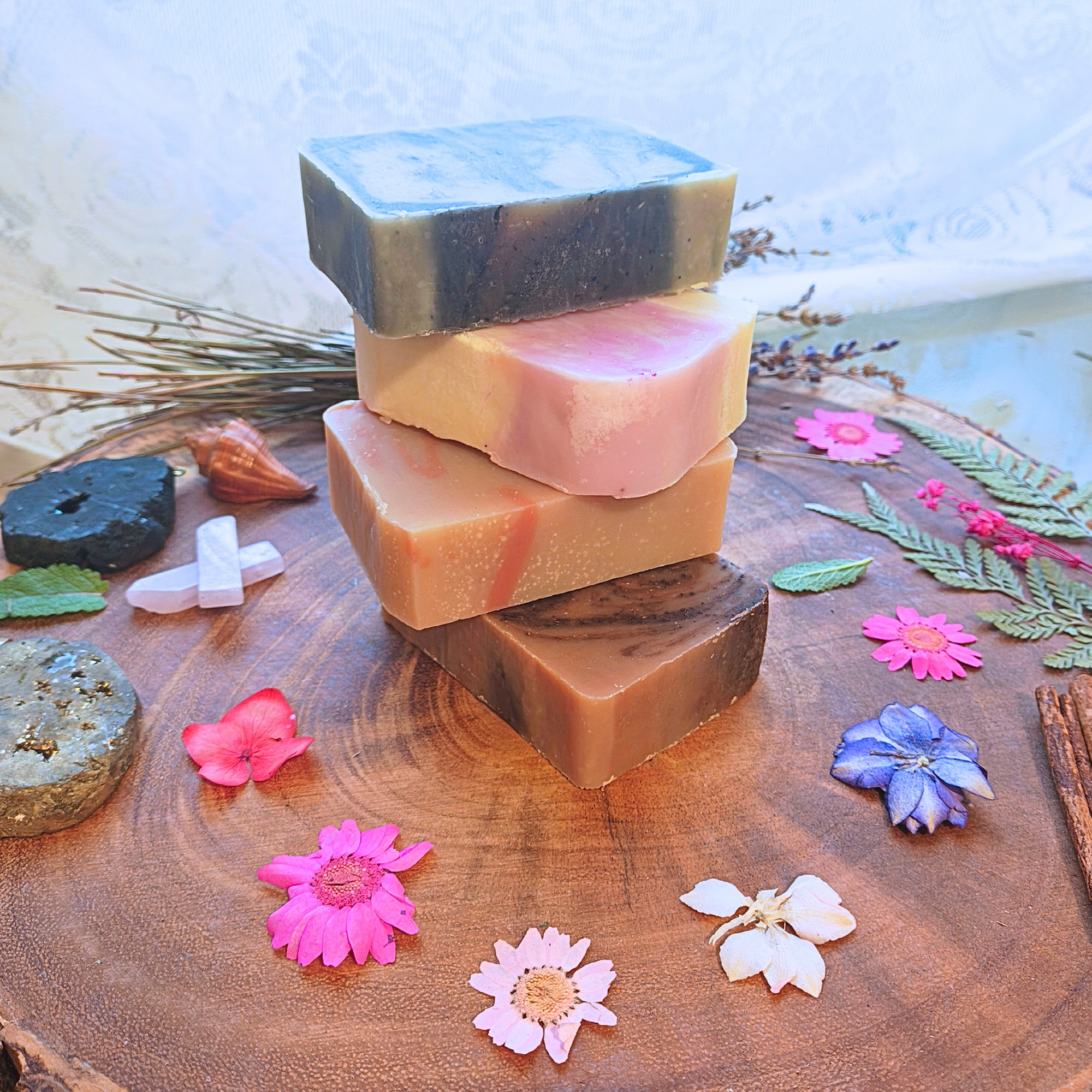 Stacked artisan soap bars with flowers, wooden background, and All Natural Body Balm.