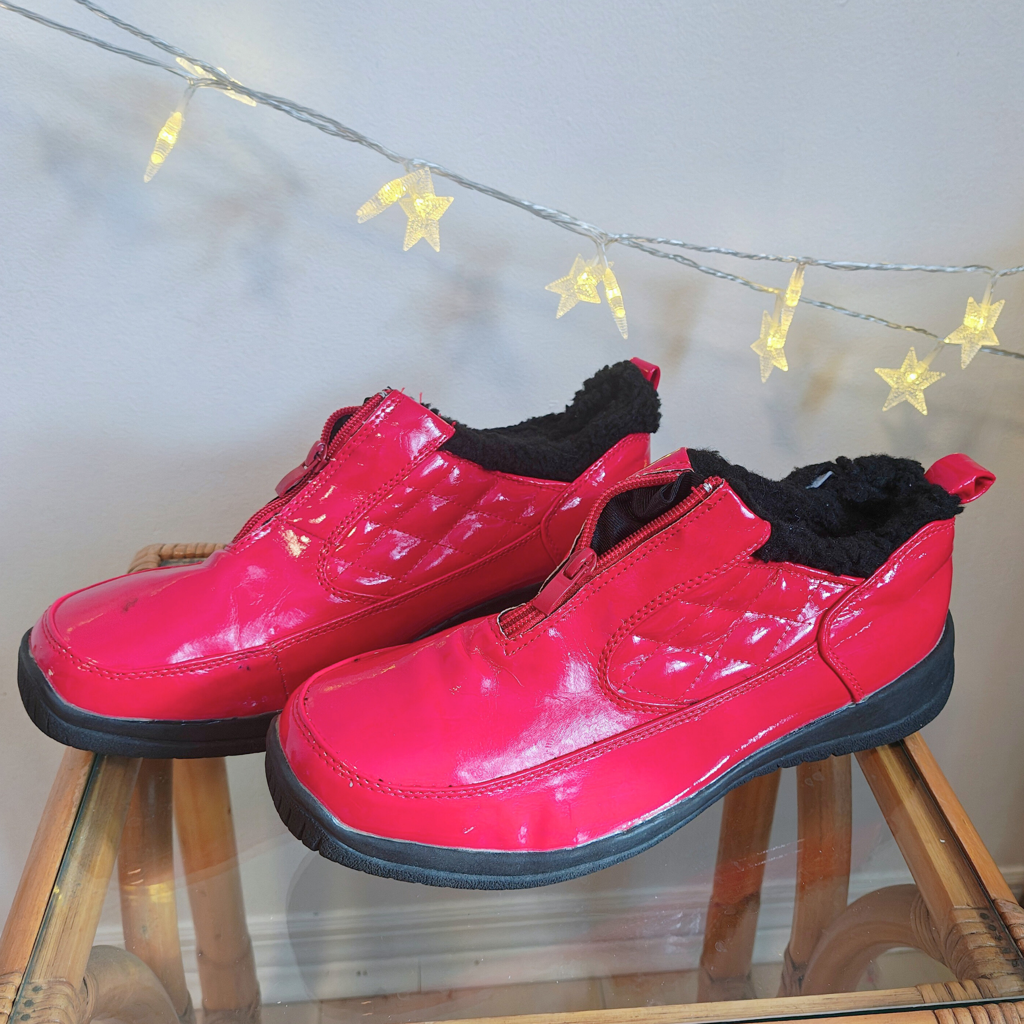 Pair of shiny red shoes on a glass table in front of lights.