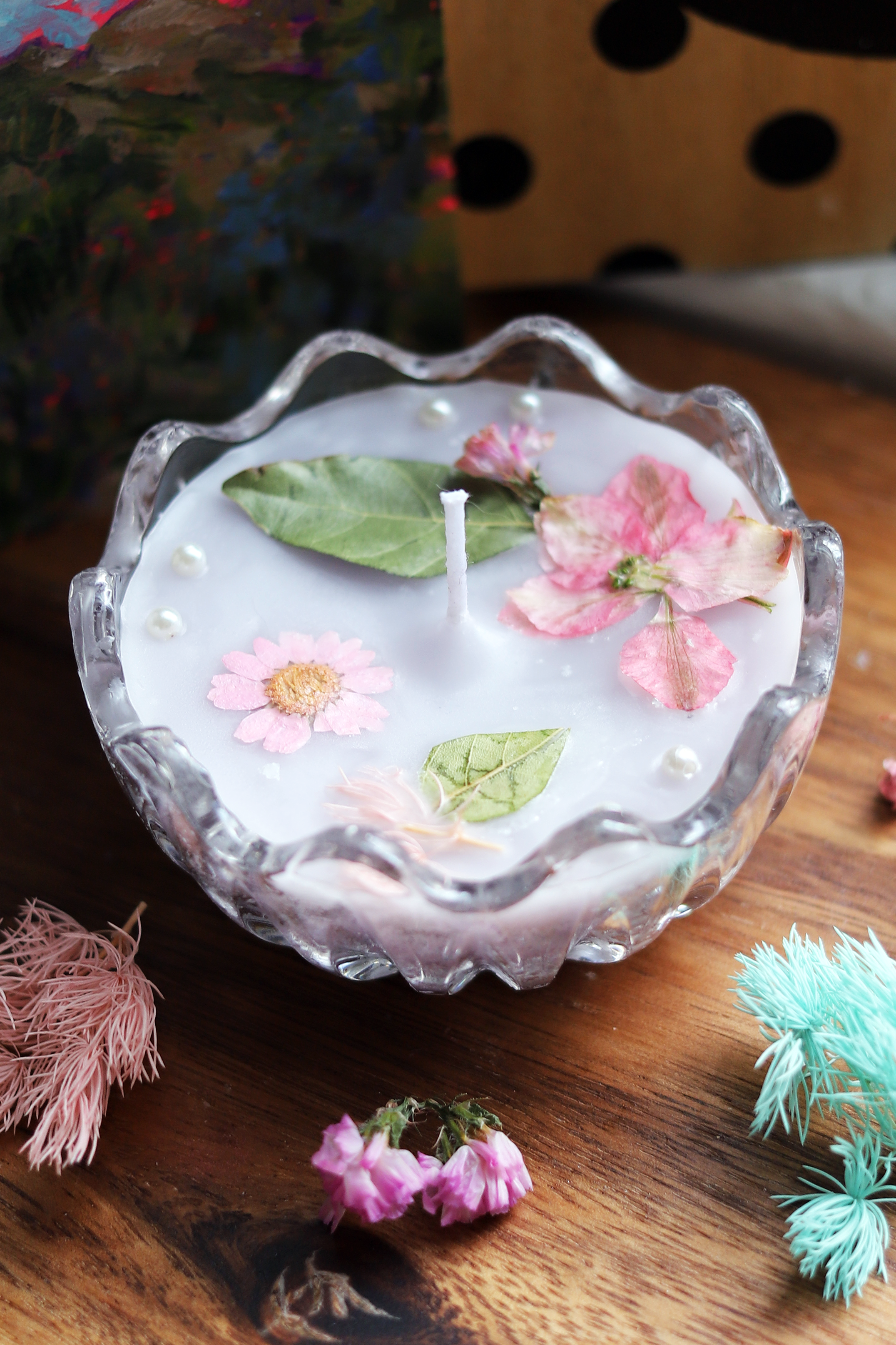 Decorative candle with dried flowers and leaves, sitting on wooden table.