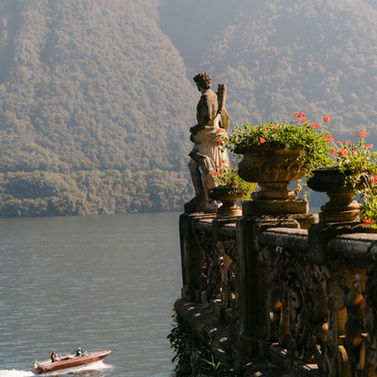 Ornate balustrade with statue overlooking lake, boat, and mountains.