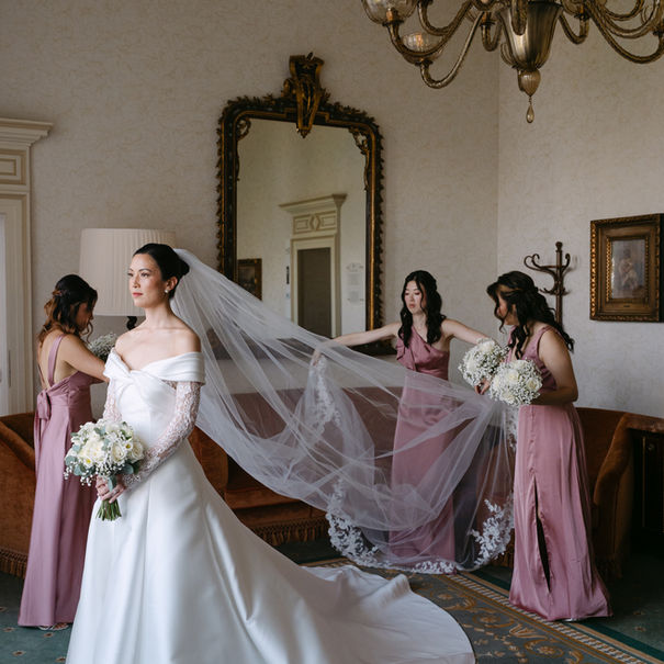Bride with bridesmaids adjusting her long veil indoors