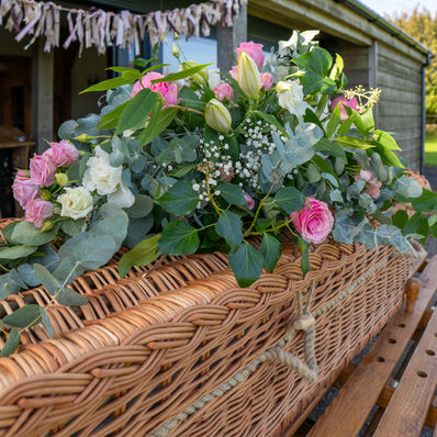Hand‑woven willow coffin titled buff petal coffin with flower arrangement - showcasing sustainable design and floral tribute