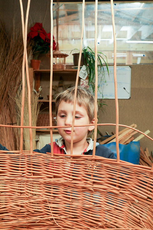 Young child weaving willow under guidance, reflecting family involvement in coffin making