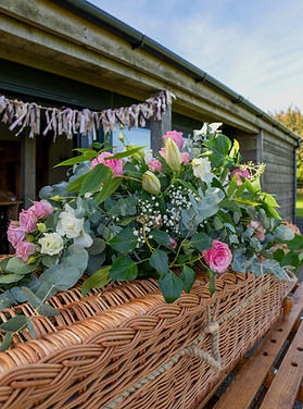 Willow coffin decorated with a vibrant floral arrangement