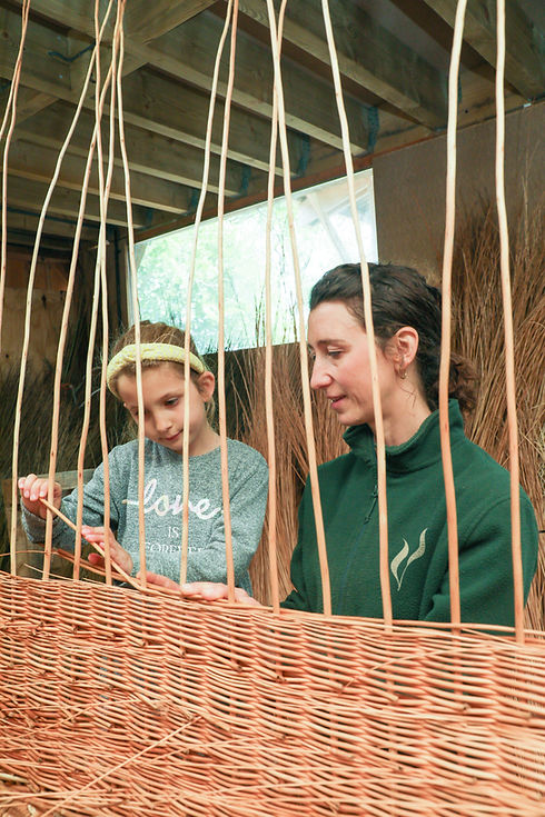 Young girl weaving willow under guidance, reflecting family involvement in coffin making