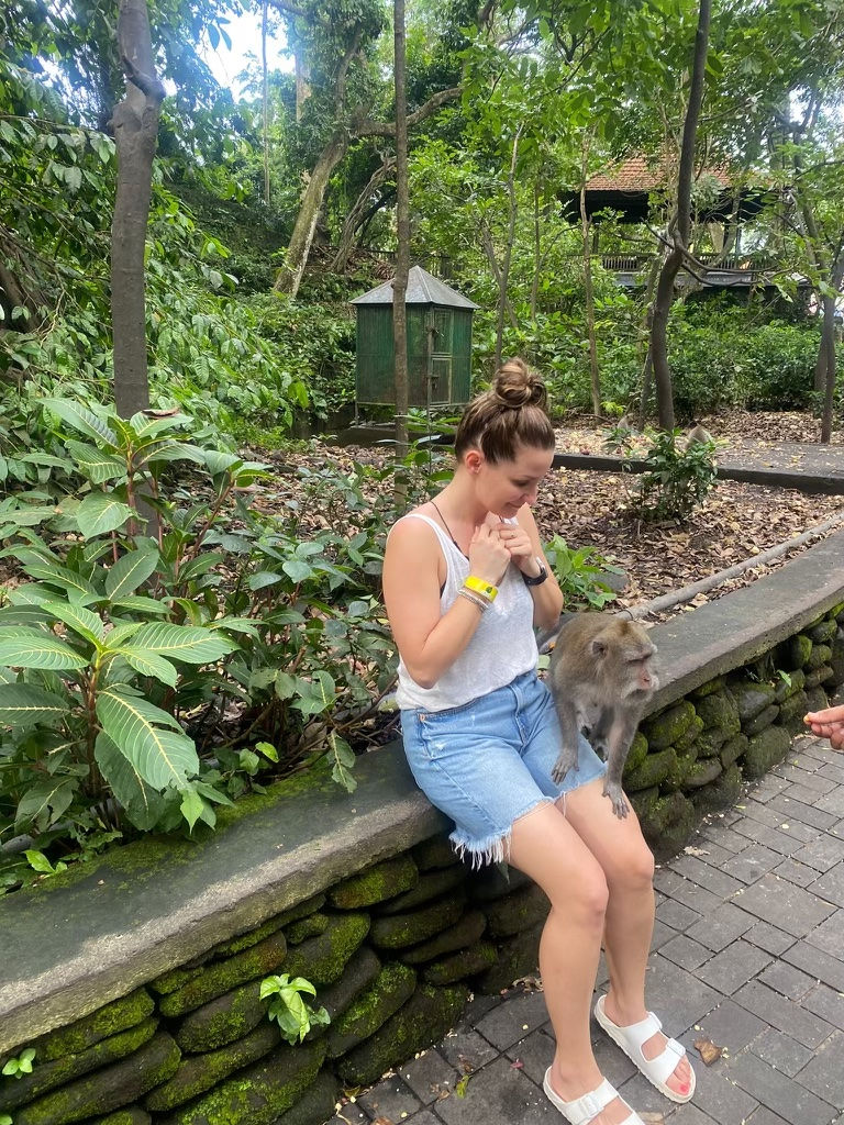 Sandra Wilczynska, owner of Prestige Beauty Bar Inc, sitting on a rock ledge at the Sacred Monkey Forest Sanctuary in Bali with a monkey climbing on her lap.
