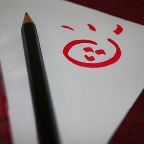 smiley face in red ink on paper with pens besides it