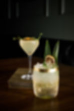Two cocktails: a martini with citrus, and a short glass with pineapple leaves.