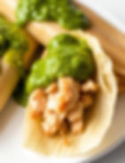 tamales with chicken inside the tamale and green sauce on top with a white background.jpg