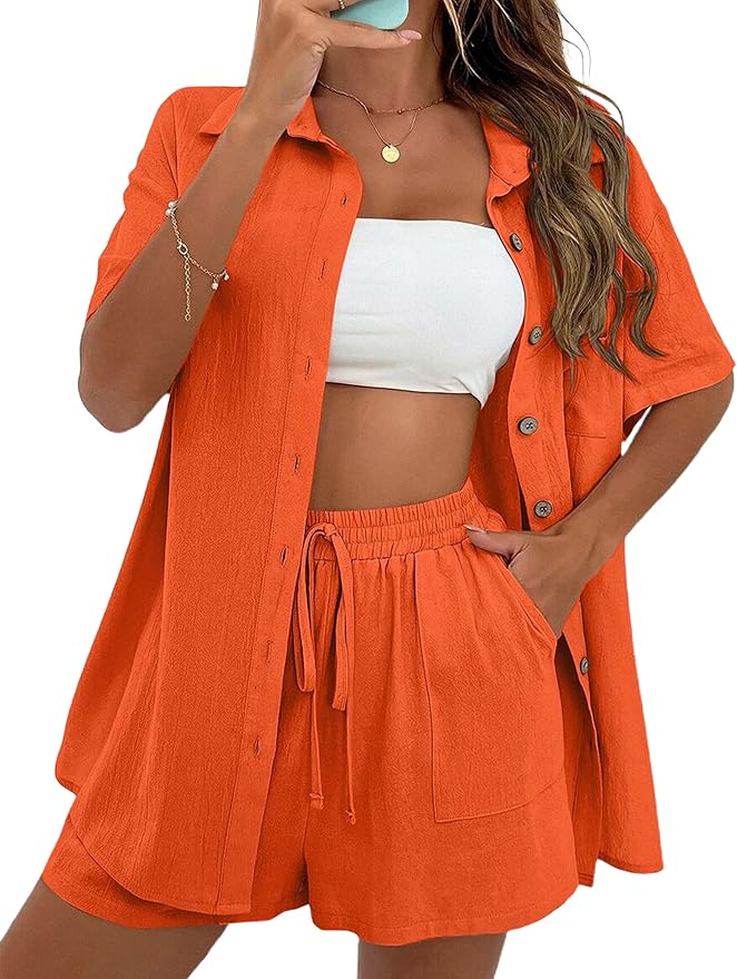 A model wearing an orange button-down shirt paired with matching orange shorts, holding a phone and posing with a casual look.