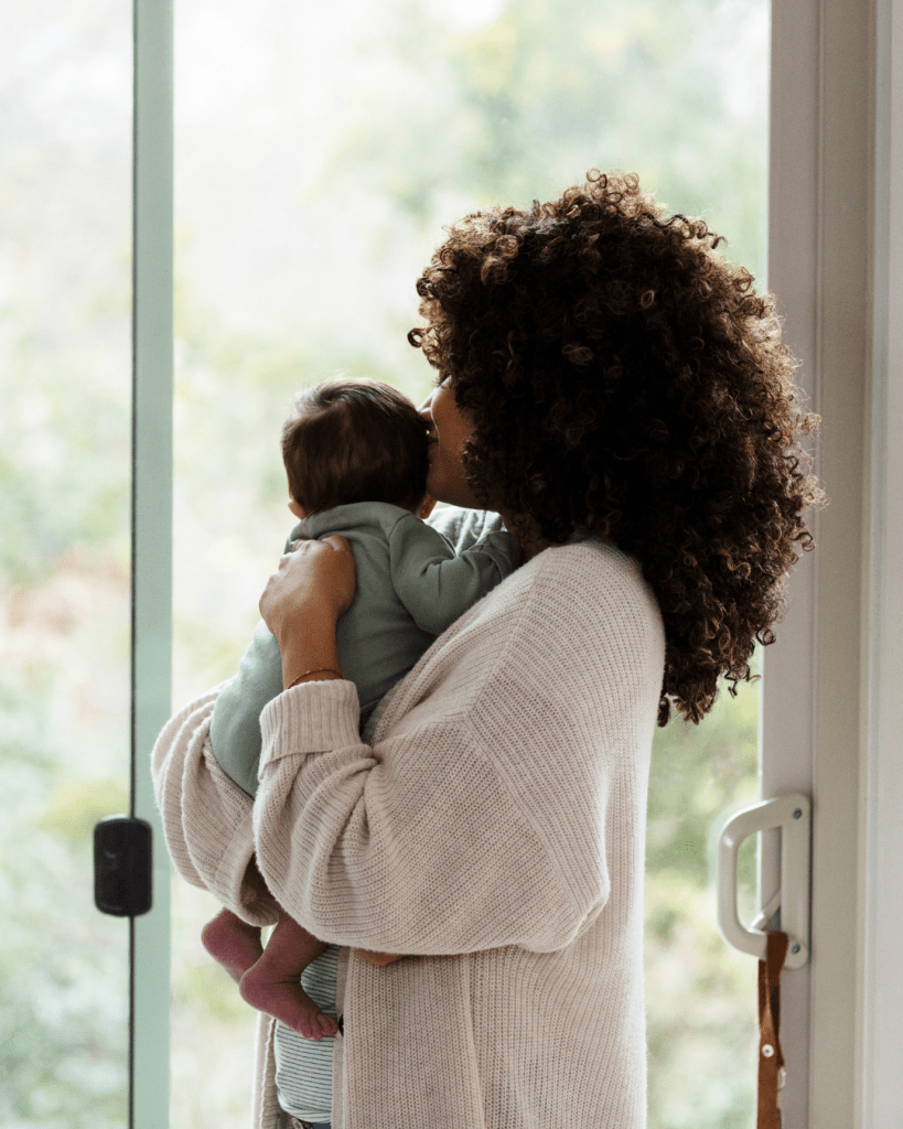 A mother holding her baby close while looking out a window, capturing a tender moment of love and connection.
