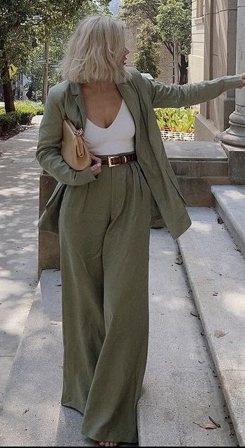 A woman wearing a light green oversized suit with wide-leg pants and a white top, holding a beige handbag while walking outdoors.