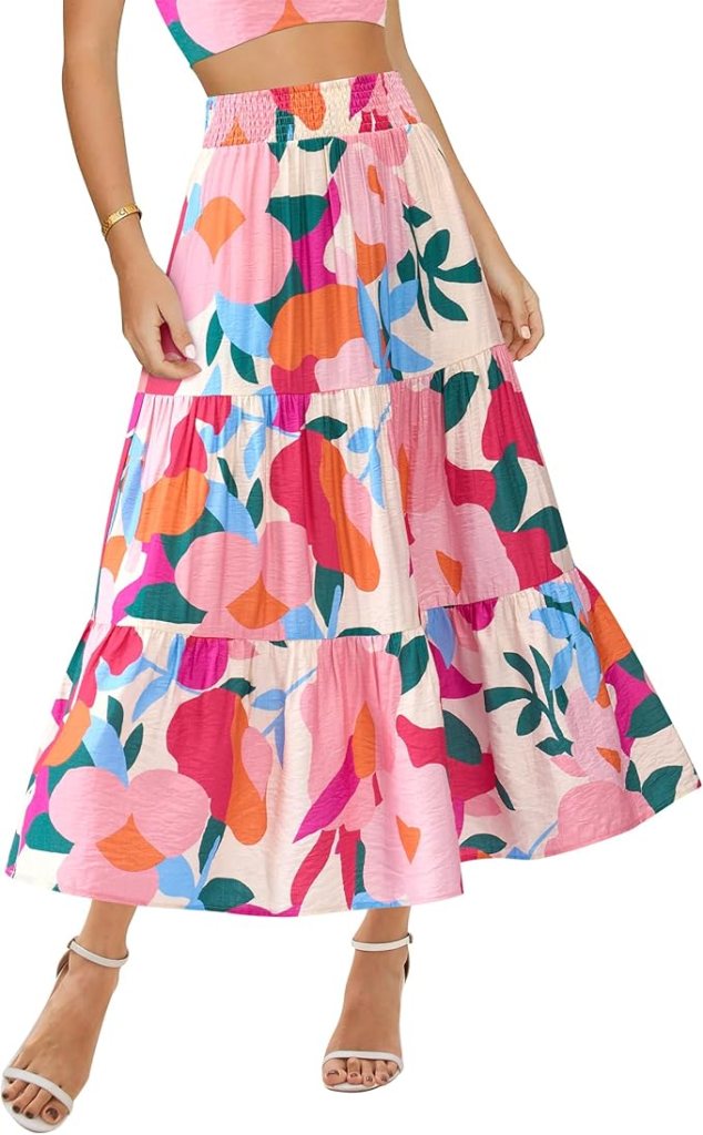 A person wearing a colorful, patterned maxi skirt featuring vibrant floral designs, paired with a matching cropped top and white strappy sandals.