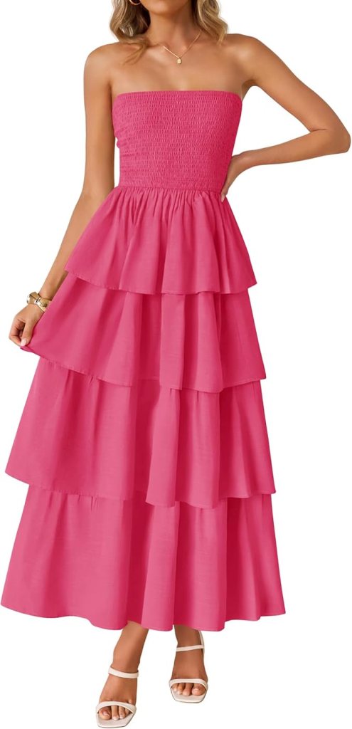 A woman wearing a strapless, tiered pink maxi dress with a smocked bodice and white sandals.