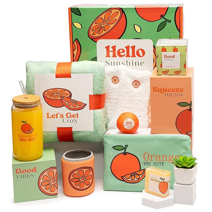 A colorful gift basket containing a cozy blanket, a bath bomb, and various items with orange-themed designs, including a candle and a jar of juice.