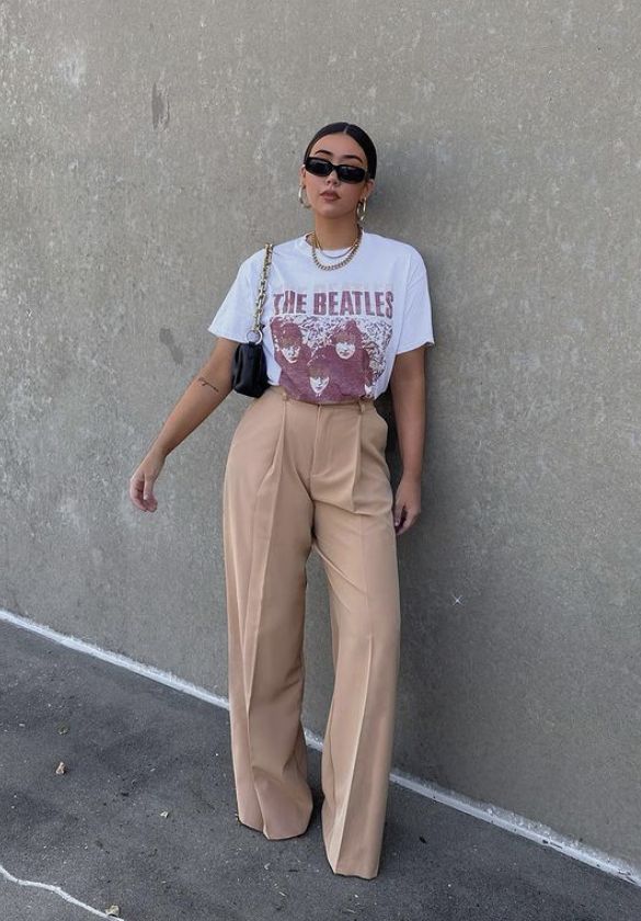 A person wearing a vintage Beatles graphic tee, beige wide-leg pants, and sunglasses, posing against a neutral wall.