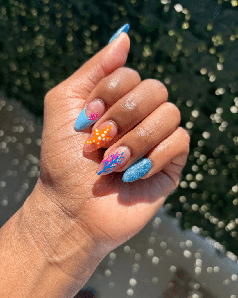 Close-up of a hand showcasing colorful DIY nail art with blue, orange, and pink designs, including starfish and coral patterns.